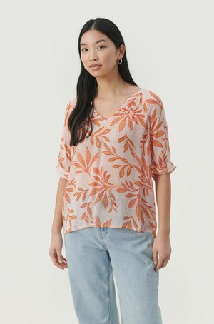 Rosa genomskinlig blus med orange bladmönster, V-ringning, korta uppvikta ärmar och en lös passform. Bärs tillsammans med ljusblå jeans.