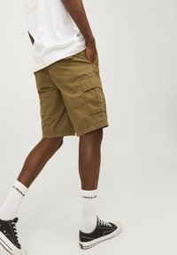 Shorts cargo kaki avec poches latérales, coupe décontractée et détails cousus, associés à des baskets noires et des chaussettes blanches.