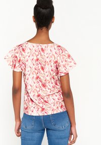 Halenka s krátkým rukávem vyrobená z měkké, lehké tkaniny s abstraktním vzorem v odstínech růžové a béžové. Má volný střih a kulatý výstřih.