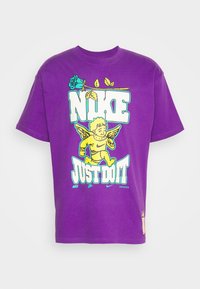 Lila bomullströja med en stor grafisk design som har "NIKE" och "JUST DO IT", tillsammans med en änglalik karaktär och blommiga detaljer. Kort ärm.