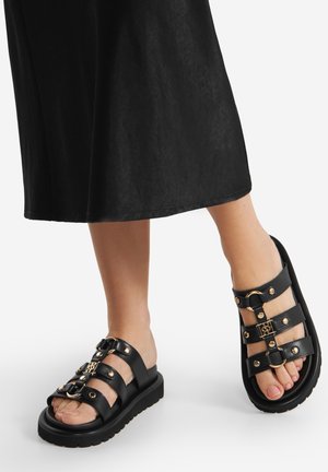 Schwarze Sandalen mit drei breiten Riemen und goldfarbenen Hardware-Akzenten. Dicke Sohle mit strukturiertem Gummi für besseren Halt, offen vorne gestaltet.