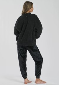 Maglione in pile nero con superficie texture, vestibilità oversized e dettaglio con bottone sulla schiena. Abbinato a pantaloni da tuta in velluto nero con polsini a coste.