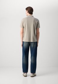 Beige polotrøye med korte ermer, detaljert søm, kombinert med mørkeblå løstsittende jeans, og beige og stripete sandaler.