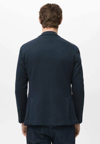 Marineblauwe blazer van een gestructureerde stof, met een enkele split, twee zijzakken en knoopmanchetten, gezien van achteren.