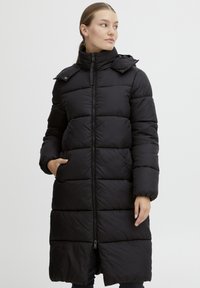 Lang svart boblejakke med kviltet design, glidelås foran, høy krage og sidelommer. Glatt tekstur og midtlengde.