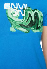 Camiseta de algodón azul con un diseño gráfico abstracto en verde y negro, y el texto "ENVII ON" en letras blancas. Mangas cortas.