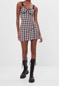 Rutig minikjol i svart och vitt med breda axelband och bustier-stil på kuporna. Matchad med svart läderstövlar som går upp till knäna och har snörning.