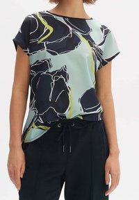 Kortärmad, ljusblå topp med svart blommönster och gröna detaljer. Tillverkad av mjukt tyg med en avslappnad passform och rundad halsringning.