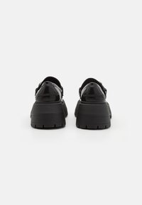 Chaussures à plateforme noires avec une finition brillante, dotées d'une semelle épaisse et d'une forme arrondie, présentant un design simple et un matériel minimal.