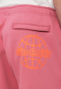 Ροζ βαμβακερά σορτς με ελαστική μέση, με πίσω τσέπη και πορτοκαλί τυπωμένο σχέδιο παγκόσμιου χάρτη με το κείμενο «Live On Air».