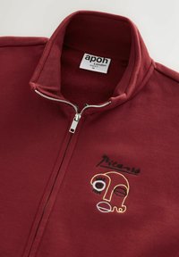 Bordeauxroter Reißverschlussjacke mit hohem Kragen, verziert mit einem gestickten abstrakten Gesicht in schwarzer, weißer und gelber Naht.