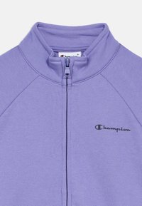 Μπλούζα με φερμουάρ σε μοβ απόχρωση, με ψηλό γιακά, κατασκευασμένη από μαλακό ύφασμα. Διαθέτει μα ύρο λογότυπο "Champion" στο αριστερό στήθος και φερμουάρ σε αντίθετο χρώμα.