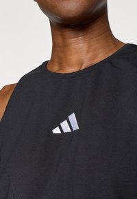 Čierny bezrukávový atletický top s okrúhlym výstrihom. Na ľavej strane sa nachádza reflexné logo so tromi pruhmi v striebornej farbe. Mäkka textúra látky.