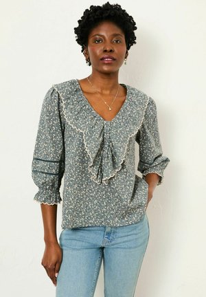 Floral-patterned blouse in blue, with a V-neck, ruffled collar, and three-quarter sleeves. Features textured fabric and cream accents.