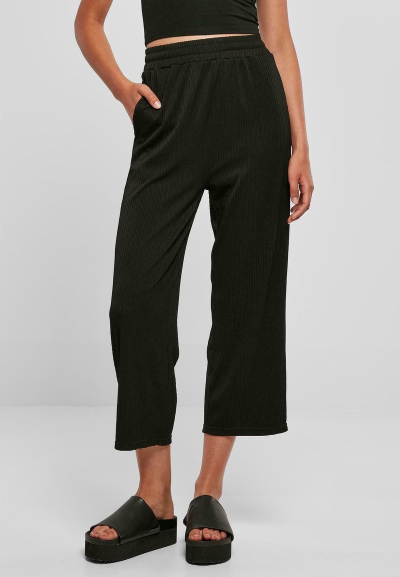 Pantalon noir côtelé à coupe décontractée, avec une ceinture élastique et des poches latérales. Associé à des sandales à plateforme noires.