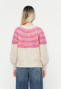 Knit sweater featuring a pink patterned upper section and cream lower part, with a relaxed fit and ribbed hem. Textured yarn throughout.