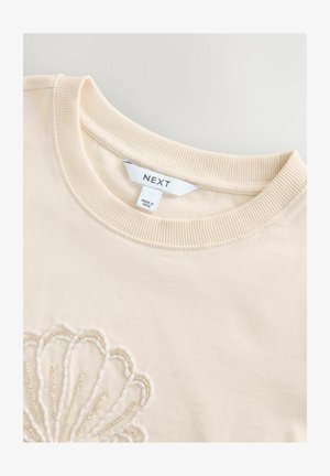 Sweatshirt od pamučne tkanine krem boje s rebrastim okruglim izrezom i složenim perlicama koje formiraju uzorak školjke na prednjem dijelu. Vidljiva oznaka brenda.