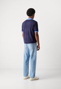 Marinblå stickad polo med ljusblå krage och ärmdetaljer. Kombineras med ljusblå jeans och vita sneakers. Minimalistisk design, avslappnad passform.