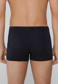 Černé fitted boxerské trenýrky s hladkým povrchem a středně vysokým pasem, z pohledu zezadu.