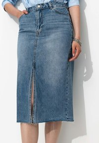 Jupe en denim bleu clair, longueur genoux avec une fente frontale. Elle présente un ourlet effiloché, cinq poches et une fermeture à bouton en argent à la taille.