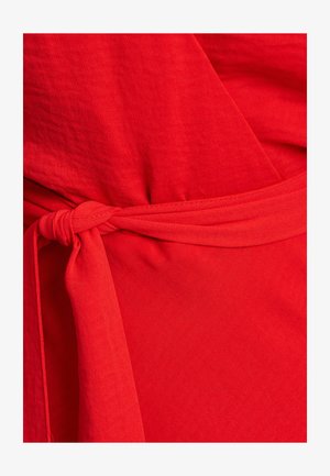 Red wrap dress with a tie belt, featuring a smooth texture and flowing fabric. The design includes a deep V-neckline and a full skirt.
