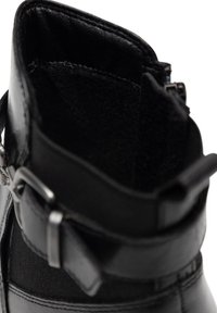 Fekete bőrből készült bokacsizma, belül puha anyaggal bélelve, oldalsó cipzárral és a külső szárán található csat díszítéssel.