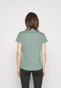 Tričko s krátkým rukávem v tlumené zelené barvě, z lehké látky, s kulatým výstřihem, hladkým povrchem a volným střihem, nošené s černými legínami.