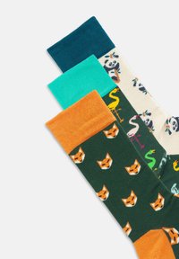 Calcetines de algodón coloridos con varios patrones: bandas en tonos azul verdoso, turquesa y naranja, y un calcetín verde con caras de zorro. Textura suave, longitud a medio pantorrilla.