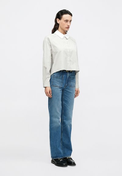 Cropped, long-sleeve shirt with a checked pattern in light gray and white, paired with high-waisted, wide-leg blue denim jeans and black shoes.