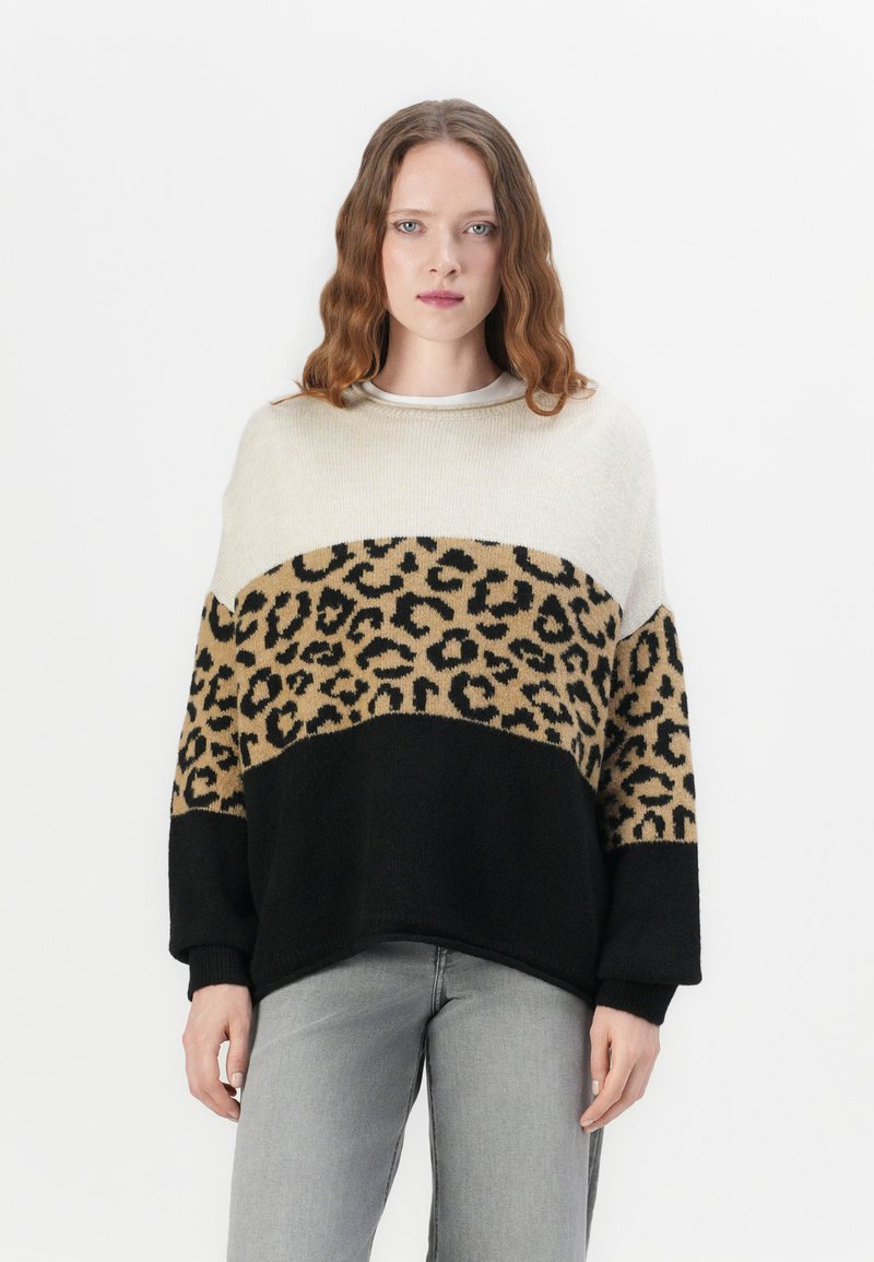 Pull en tricot avec imprimé léopard crème et beige, et sections noires. Il présente un col rond et des manches longues avec des poignets côtelés.