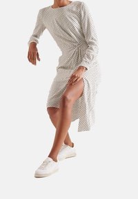 Sukienka do kolan z białego materiału z czarnym abstrakcyjnym wzorem, z długimi rękawami, skręconym detalem po boku oraz rozcięciem na wysokości uda.