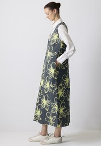 Ärmeloses, dunkelgraues Kleid mit neon-gelbem Blumenmuster, Seitentaschen und einer entspannten Passform, kombiniert mit weißen Sneakers.