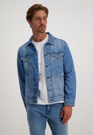 Lichtblauwe spijkerjack met een klassieke pasvorm, knoopsluiting, borstzakken en een puntkraag. Draagt over een wit T-shirt.