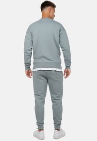 Felpa grigia chiara e pantaloni della tuta in misto cotone, con polsini e orlo a costine. Sneakers bianche completano l'outfit.