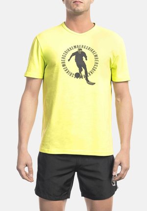 Neon yellow cotton T-shirt with a black graphic print of a soccer player. Round neck and short sleeves. Paired with black shorts.