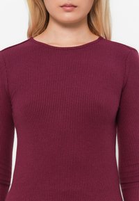 Haut à manches longues bordeaux à côtes avec un col rond. Design ajusté, fabriqué à partir d'un tissu texturé, mettant en valeur des détails de côtes verticales.