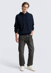 Mörkblå hoodie med dragsko, bärs med grå jeans och vita sneakers. Har en avslappnad passform samt ribbade muddar och fåll.