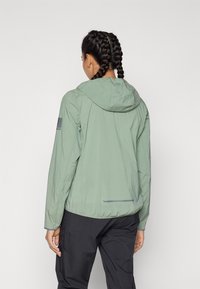 Helle grüne Windjacke mit Kapuze, minimalistisches Design, elastische Bündchen und ein reflektierender grauer Akzent am Saum.
