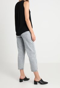 Top negro sin mangas, jeans de talle alto gris claro, mules negros de punta abierta con tacón grueso; diseño sencillo, ajuste casual.