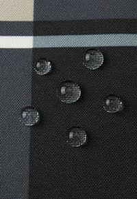 Krople wody na ciemnej tkaninie w kratę o teksturowanej powierzchni, z szarymi, czarnymi i delikatnymi niebieskimi paskami.