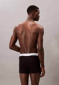 Schwarze Baumwoll-Boxershorts mit einem weißen Bündchen, das das Branding "Calvin Klein" zeigt, von hinten betrachtet, die Haut des Models ist sichtbar.