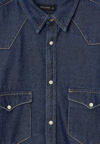 Camicia di jeans di colore blu scuro con colletto a punta, chiusura con bottoni frontali, due taschini sul petto e dettagli di cucitura dorati. Taglia L.