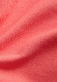 Makroaufnahme eines weichen, korallrosafarbenen Stoffes mit sichtbarer Webstruktur und sanften Falten, die Licht- und Schattenmuster erzeugen.