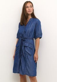 Denim haljina duboke plave boje s ovratnikom, dugmadi sprijeda, kratkim rukavima i dva prednja džepa. Ima strukirana pojas s mašnom.