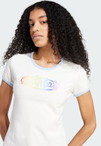 Biely priliehavý tričko s svetlomodrým rebrovaným výstrihom a manžetami rukávov. Obsahuje farebný, irizujúci logotyp "Adidas" naprieč hrudníkom.