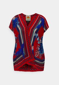 Haut rouge à manches courtes avec des motifs floraux et d'oiseaux bleus, décolleté en V et accents g éométriques dans des couleurs contrastées. Tissu léger.