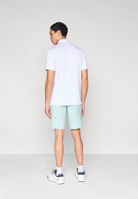 Svetlofialová polokošeľa s krátkymi rukávmi, skombinovaná s mentolovozelenými šortkami. Oblečenie je doplnené bielymi športovými topánkami a členkovými ponožkami.