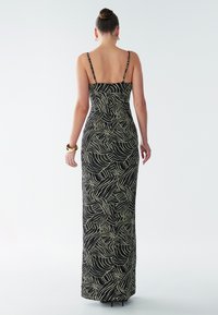 Vestido maxi estampado en negro y dorado con tirantes finos, diseño ajustado y textura suave, que muestra una silueta fluida.