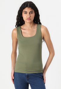 Top sans manches vert olive avec un décolleté carré, fabriqué dans un tissu lisse et extensible conçu pour un ajustement près du corps. Associé à un jean en denim foncé.