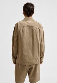 Oversized beige blouse met een kraag, met een gladde textuur en verlaagde schouders, gecombineerd met bijpassende shorts voor een gecoördineerde uitstraling.